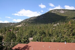 A mountain landscape with a red-roofed building in the foreground and a forested hill in the background. - Timber Creek Chalet (Estes Park)