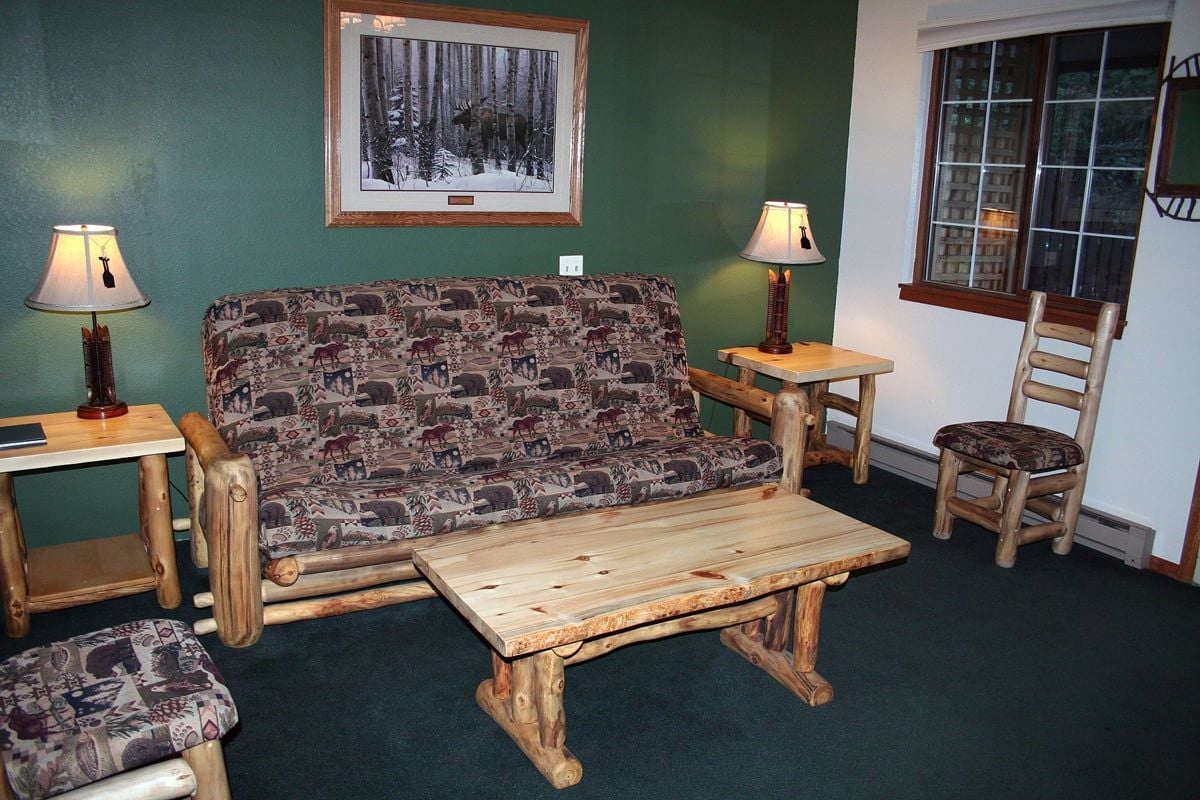 A cozy room with a patterned sofa, a wooden coffee table, a small wooden table, a chair, and two lamps.