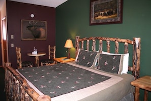A room with a bed, a wooden headboard, a small table with a lamp, and a painting on the wall. - Timber Creek Chalet (Estes Park)