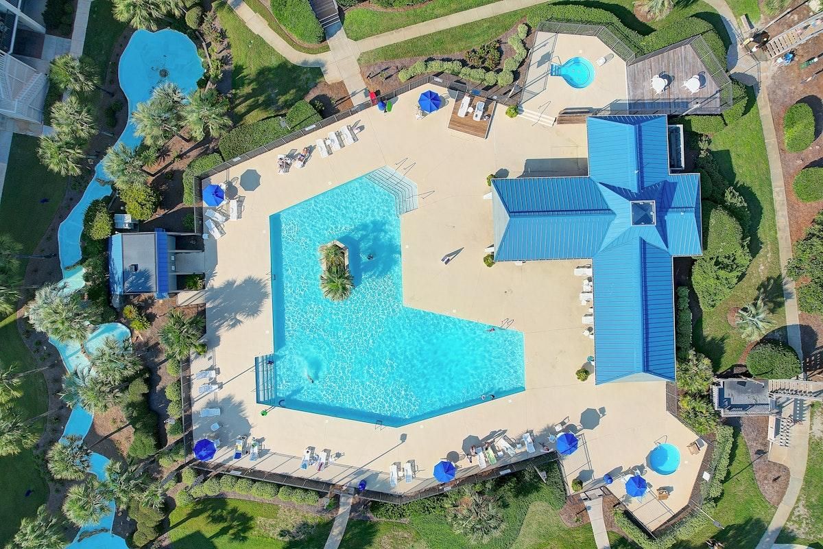 A large swimming pool with a sunken center, surrounded by lounge chairs and umbrellas, with a building featuring a blue roof in the background.