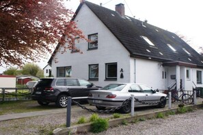 A two-story house with a white exterior and a dark roof. There are two cars parked in front, one of which is chained to a post. - Holiday apartment with 3 bedrooms (Maasholm)