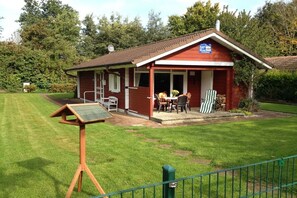 A small red building with a porch, a table and chairs outside, and a sign on the building. - Holiday home House 105 (Damp)