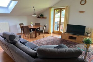 Un salon comprenant un canapé, un téléviseur, une table à manger, des chaises et une fenêtre avec des rideaux.