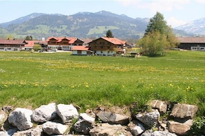 A hotel with multiple buildings, a grassy field with yellow flowers, and mountains in the background. - Holiday apartment with 2 bedrooms (Ofterschwang)