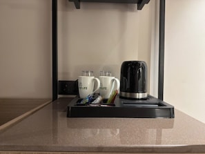 En kaffestation med två vita muggar, en svart elektrisk vattenkokare och ett bricka med diverse föremål.