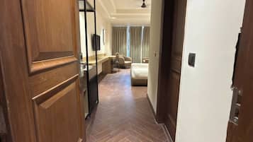 Pasillo de hotel con una puerta de madera identificada con el número '104', una zona de estar con sofá y sillones, y una cama al fondo.