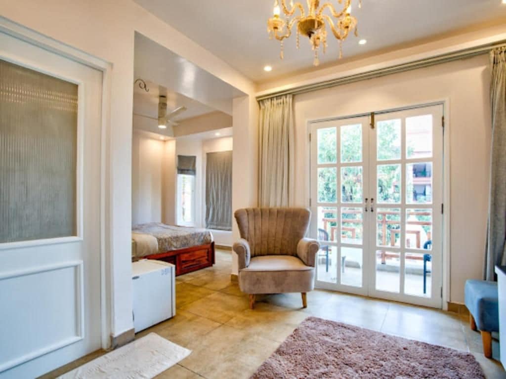 Una habitación amplia con un gran ventanal corredero que da a un espacio exterior, un sillón cómodo, una cama con cabecera y un mueble blanco pequeño.