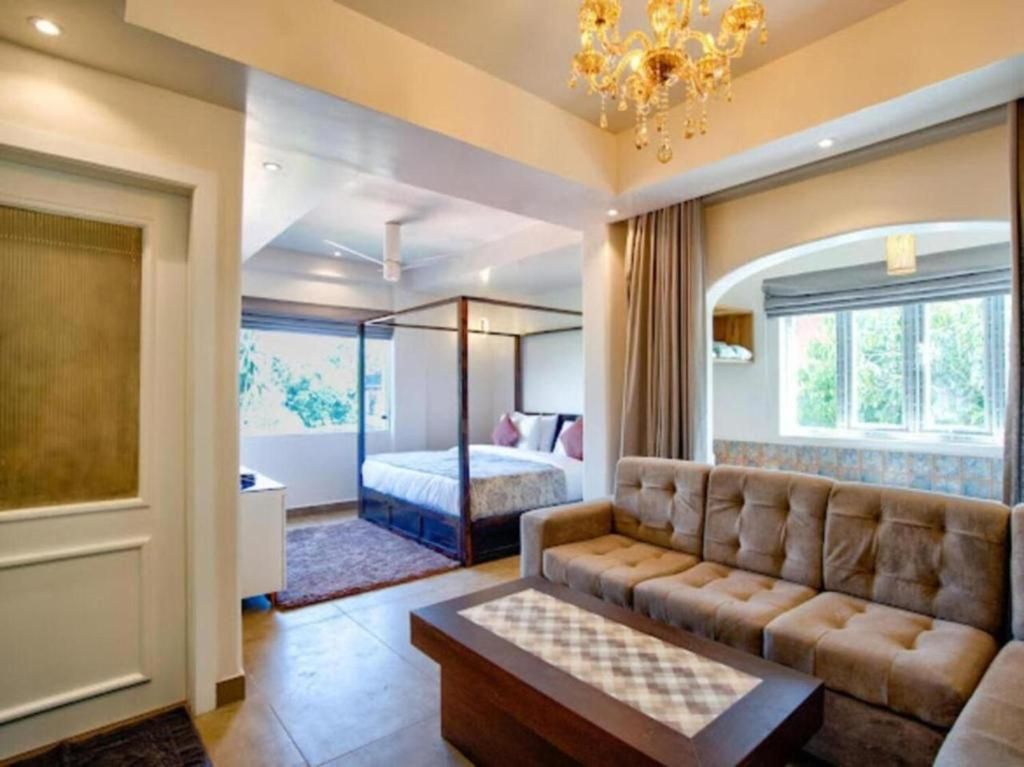 Habitación de hotel con cama con dosel, sofá, mesa de centro y una ventana grande con cortinas.