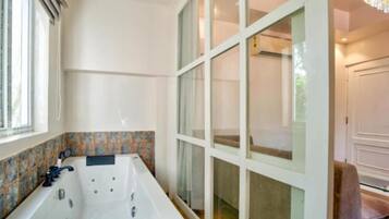 A bathroom with a large bathtub, a window, and a door leading to another room.