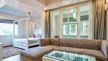 Een moderne woonkamer met een glazen salontafel, een beige bank en een bed met een witte hoofdbord.