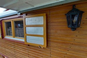 Pared exterior de madera con una ventana y un farol colgante.