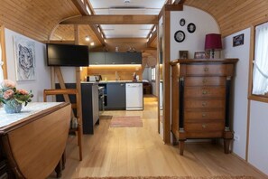 A compact kitchen with a built-in dishwasher, wooden cabinets, and a flat-screen TV mounted on the wall. - Circus wagon "Loge1" (Kappel-Grafenhausen)
