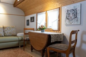 A cozy room with a wooden ceiling, a dining table with chairs, a sofa, and a window with curtains. - Circus wagon "Loge1" (Kappel-Grafenhausen)