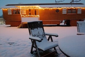 A wooden building with a covered porch area, a chair with snow on it, and a table also covered in snow. - Circus wagon "Loge1" (Kappel-Grafenhausen)