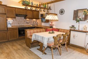 Een keuken met houten kastjes, een eettafel met stoelen, een koffieapparaat en een hanglamp.