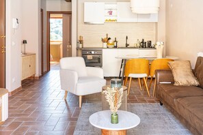 Ein modernes Wohnzimmer mit einer Couch, Sesseln, einem Couchtisch und einer Küchenzeile inklusive Herd und Schränken.