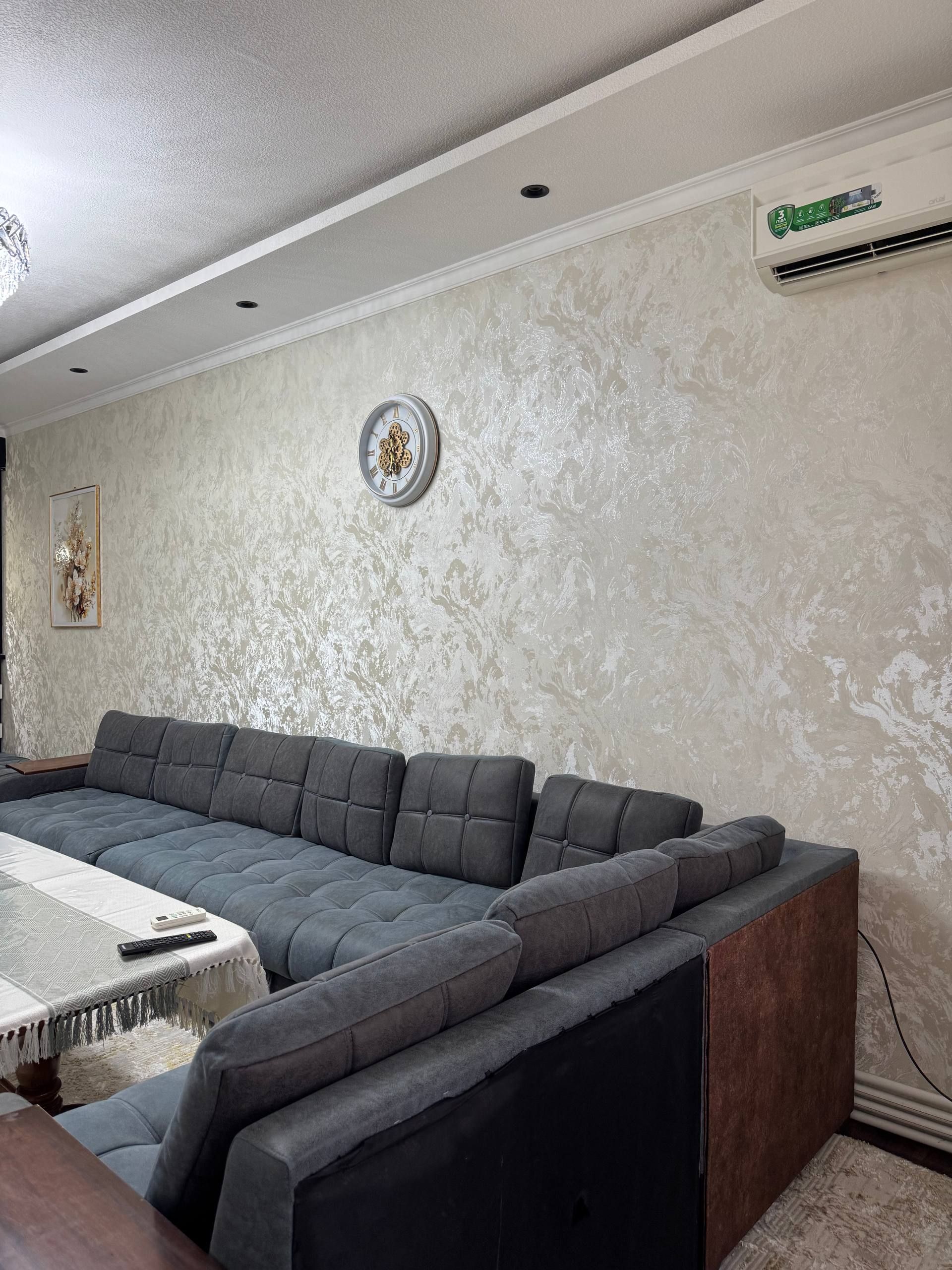 En moderne stue med en hjørnesofa, et ur og en aircondition på væggen.