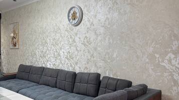 En moderne stue med en hjørnesofa, et ur og en aircondition på væggen.