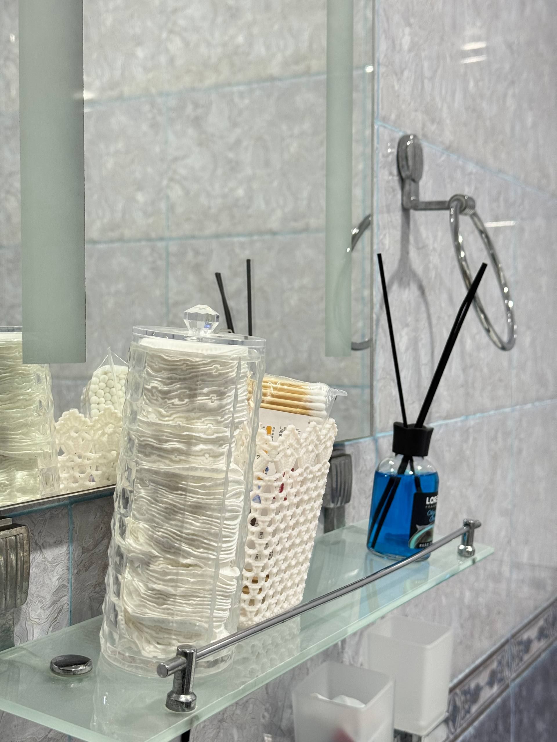 Een badkamer met een glazen plankje met toiletartikelen, een spiegel en een handdoekhouder.