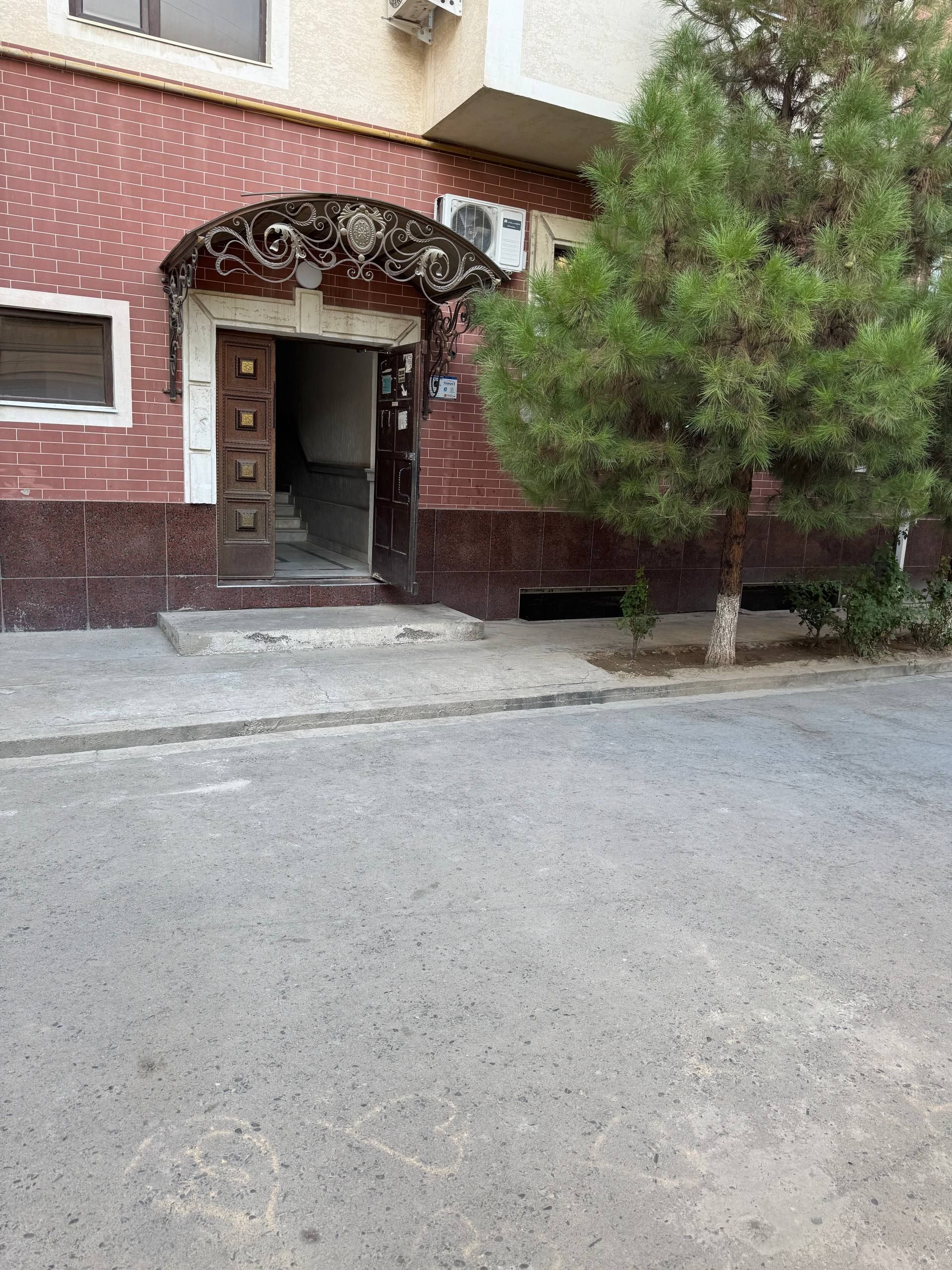 A building entrance with a decorative archway, a tree in front, and a clear sky.