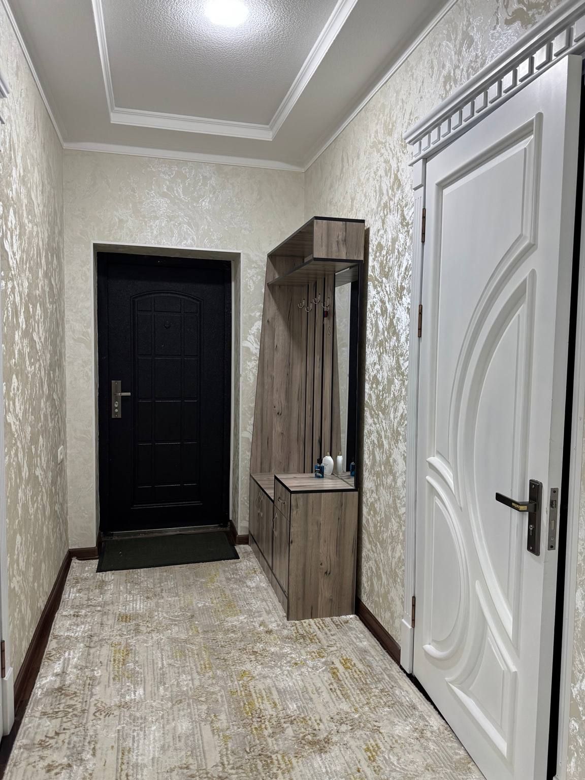 A hallway with a black door, a wooden cabinet with a mirror, and a white door with a decorative handle.
