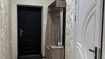 A hallway with a black door, a wooden cabinet with a mirror, and a white door with a decorative handle.