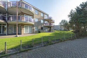 A multi-story residential building with balconies, a paved driveway, and a grassy area. - Modern 5-Guest Holiday Apartment with Balcony (Julianadorp aan Zee)