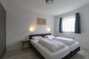 Ein modernes Schlafzimmer mit einem Bett, Nachttischen, einer Wandlampe und einem Fenster mit Vorhängen.