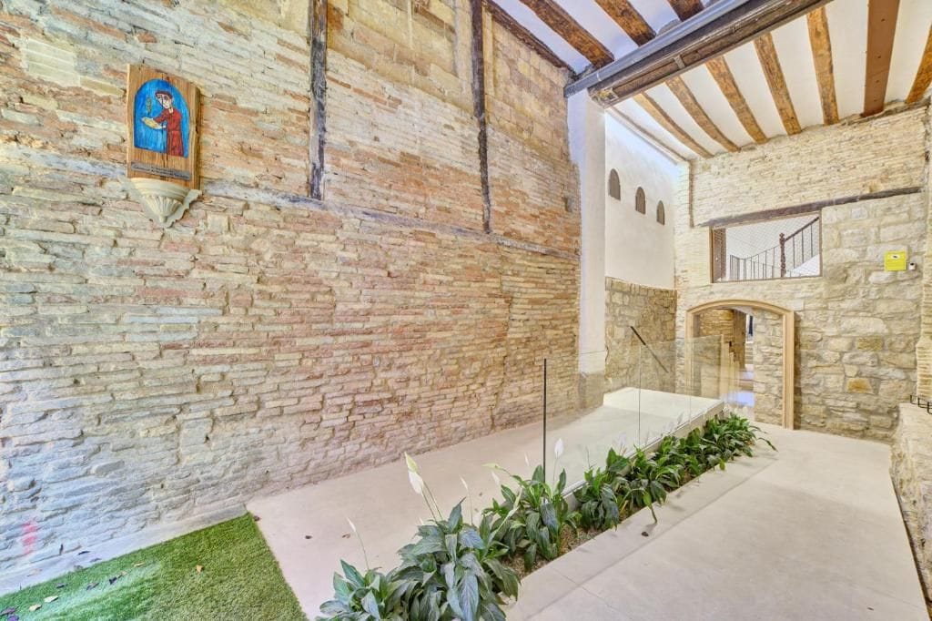 A stone interior with a wooden ceiling, a staircase, and a wall-mounted light fixture.