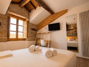 Un dormitorio con una cama, televisor, una escalera de madera y una pared de piedra.