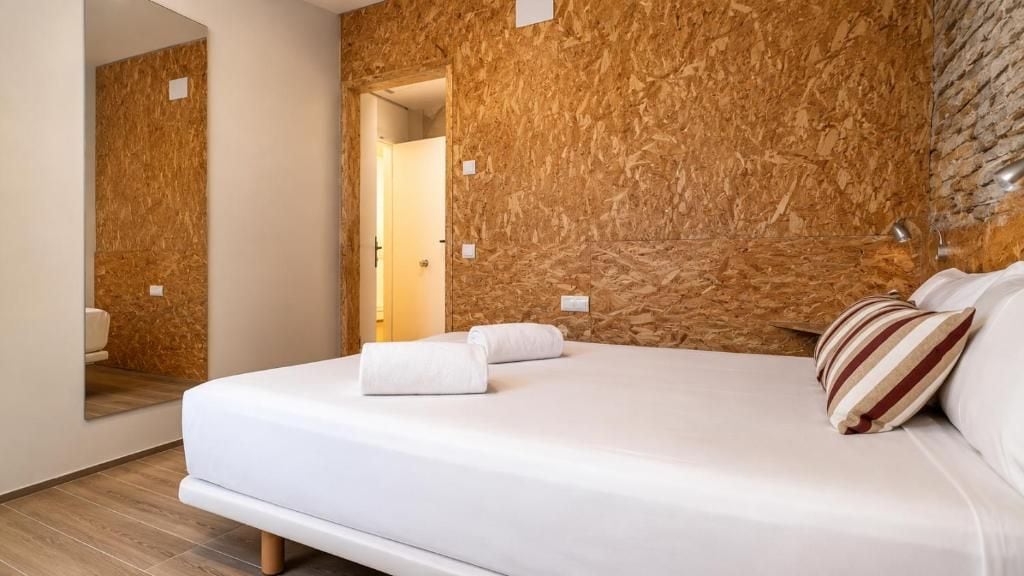 A modern hotel room with a wooden textured wall, a neatly made bed with white linens, and a visible bathroom door.