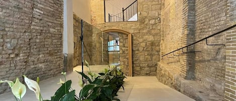 A stone-walled corridor with a glass railing and a staircase leading to an upper level.