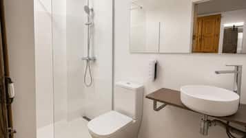 A modern bathroom with a glass-enclosed shower, a toilet, a sink, and a mirror.