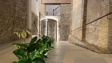 A corridor with brick walls, a concrete floor, and a staircase leading to an upper level.