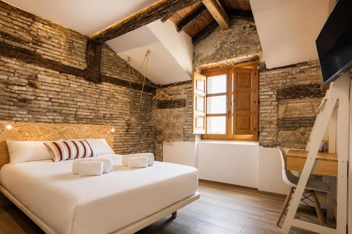 Un dormitorio con cama, un escritorio de madera, televisor y ventana con vistas al exterior.