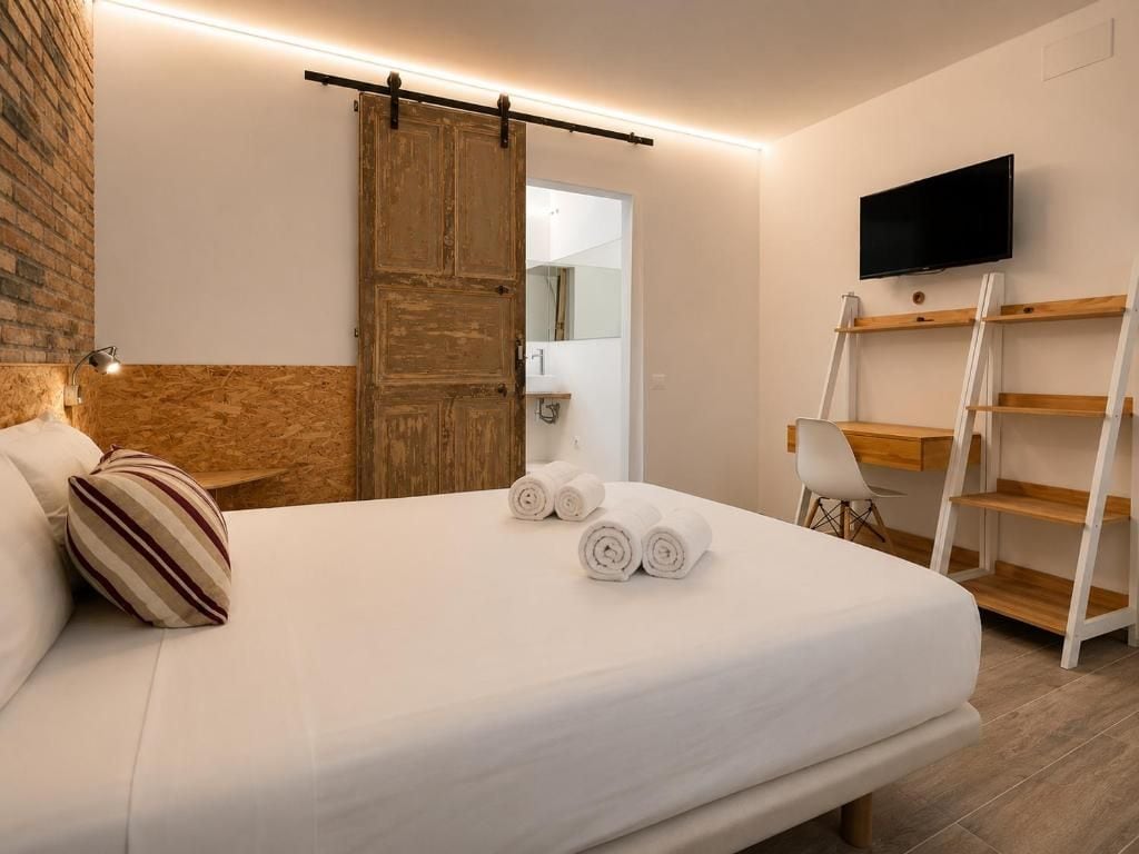 Habitació d'hotel amb un llit, una porta de fusta, una televisió i una taula amb prestatges.