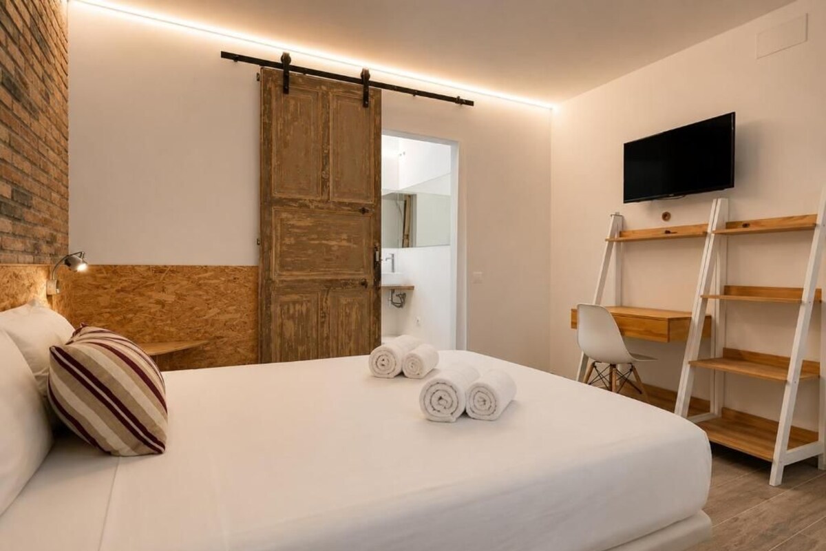 Habitación de hotel con cama, puerta de madera, televisión y escritorio con estantes.