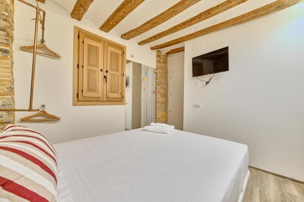 Une chambre à coucher avec un lit, des poutres en bois, un téléviseur et un luminaire suspendu.