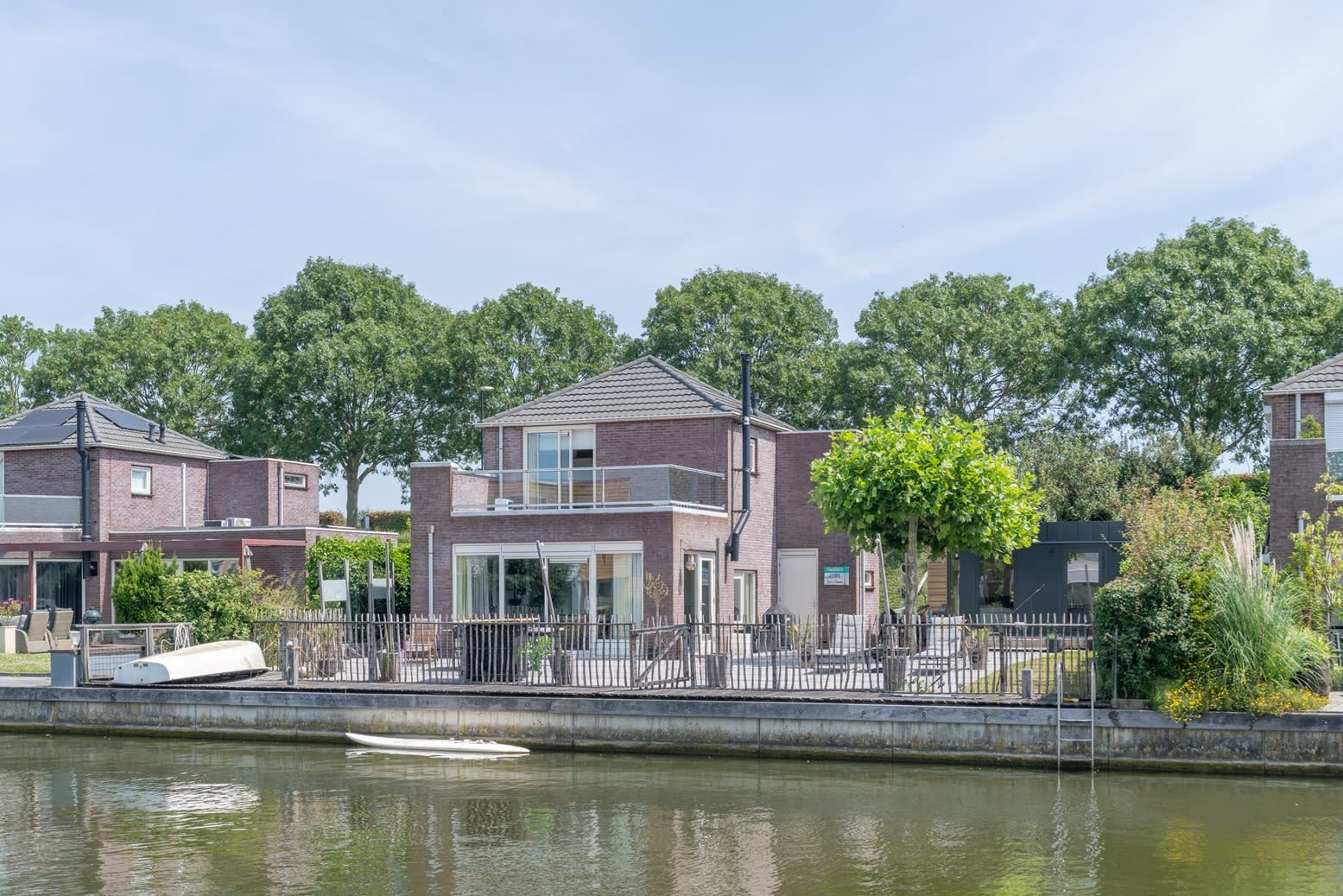 Een woonwijk met huizen aan een gracht, met een modern tweegezinshuis met balkon en plat dak.