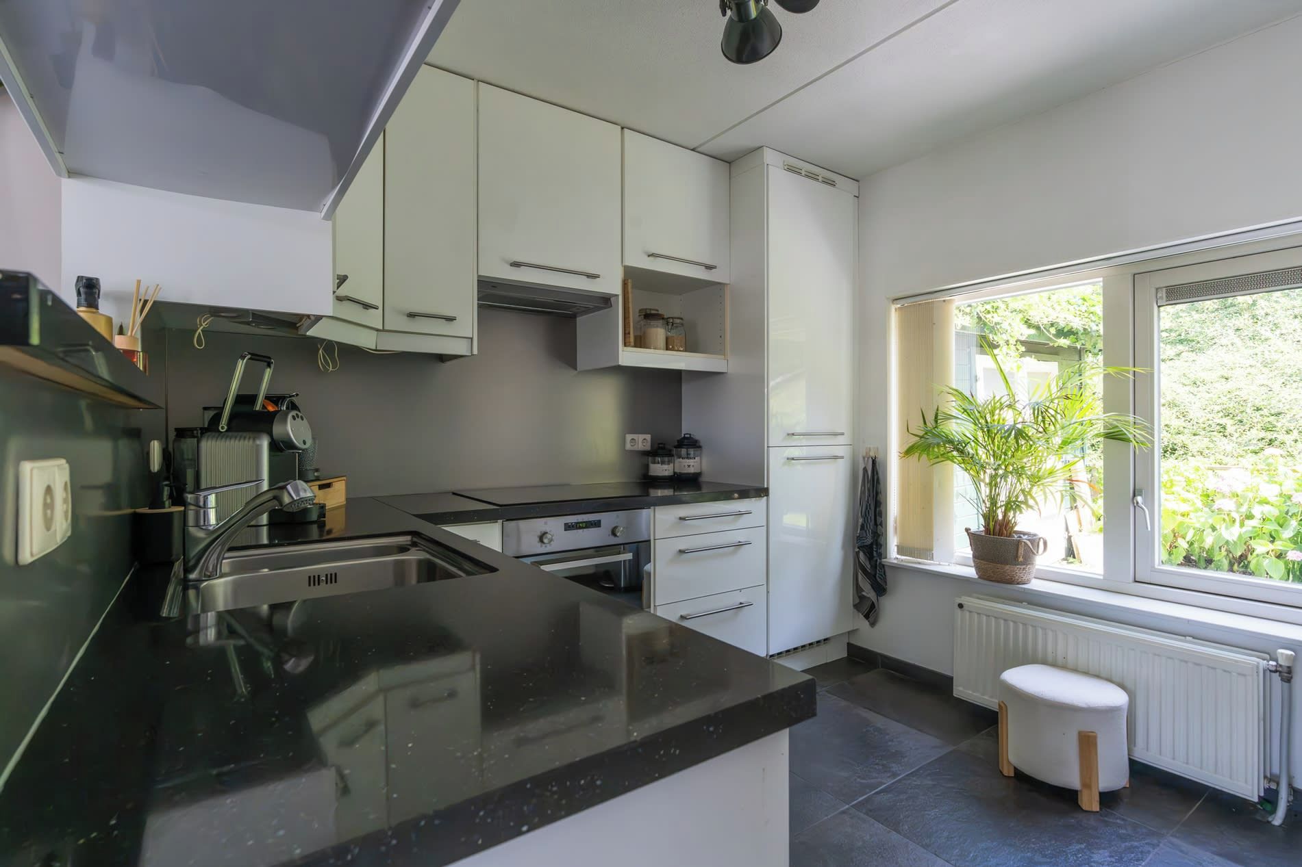 Een moderne keuken met witte kasten, een zwart aanrecht en een raam met uitzicht op groen.