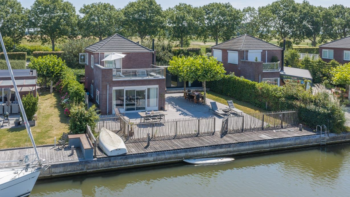 Een wooneiland met een steiger, een overdekt terras en een aangelegde tuin.