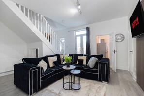 A modern living room with a black sectional sofa, a small round table, and a staircase. - 4 Bed Contractor House in Sunderland, Free Parking, AH Urban Stays (Sunderland)