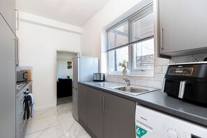 A modern kitchen with a built-in dishwasher, a stainless steel sink, and a window with blinds. - 4 Bed Contractor House in Sunderland, Free Parking, AH Urban Stays (Sunderland)