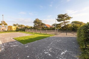 A paved courtyard with a grassy area, a wooden fence, and a gated entrance. - Luxurious home behind the dunes of Julianadorp (Julianadorp)