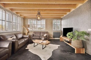 A modern living room with a leather sofa, a coffee table, and a TV. - Luxurious home behind the dunes of Julianadorp (Julianadorp)
