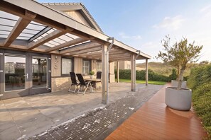 A covered outdoor patio with a table and chairs, a potted plant, and a view of the surrounding landscape. - Luxurious home behind the dunes of Julianadorp (Julianadorp)