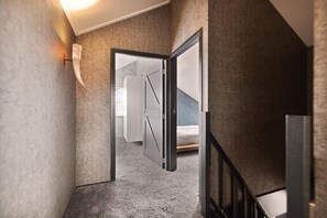 A hallway with a carpeted floor, a door leading to a bedroom, and a staircase with a handrail. - Luxurious home behind the dunes of Julianadorp (Julianadorp)