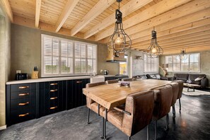 A modern kitchen with a wooden ceiling, a central island with leather seating, and large windows with blinds. - Luxurious home behind the dunes of Julianadorp (Julianadorp)