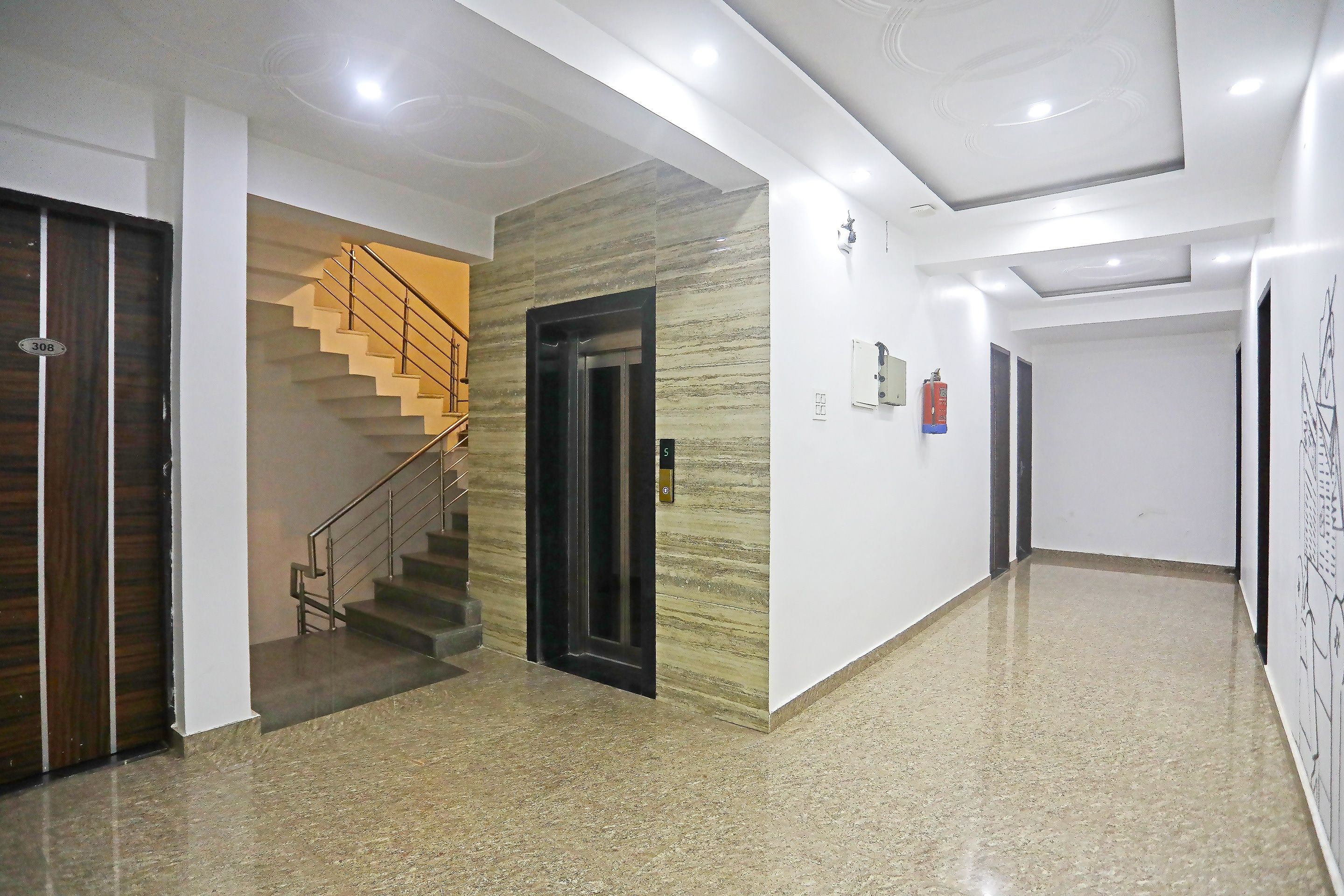 Un pasillo de hotel con suelo de mármol, una escalera con barandillas de metal y un extintor de incendios fijado a la pared.