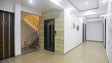 Un pasillo de hotel con suelo de mármol, una escalera con barandillas de metal y un extintor de incendios fijado a la pared.
